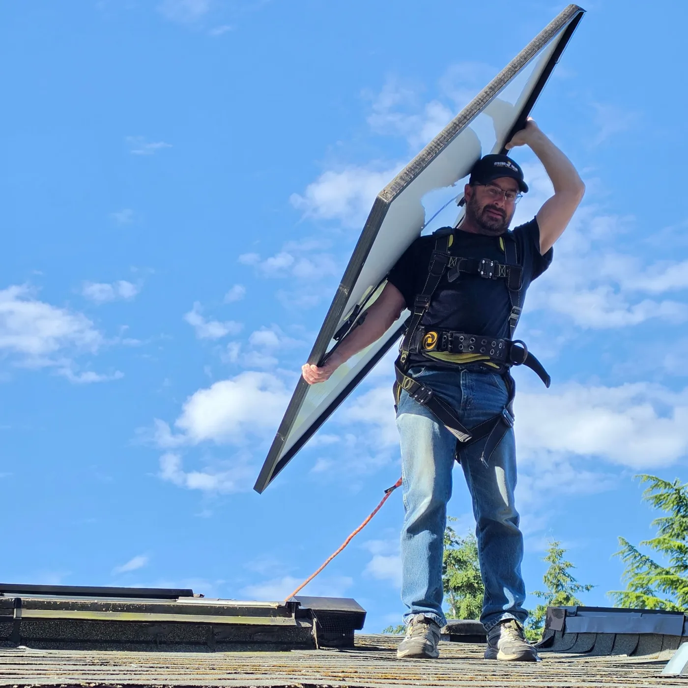 A crew member carrying a solar panel off a roof during a panel removal